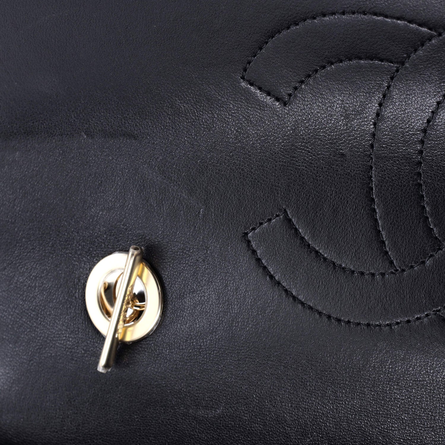 Close-up of a black leather classic Chanel handbag with black stitching, gold clasp and logo.
