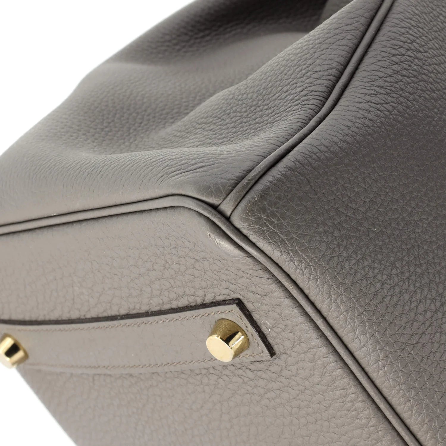 Close-up of the underside of a gray Hermes Birkin leather handbag with gold hardware on a white background