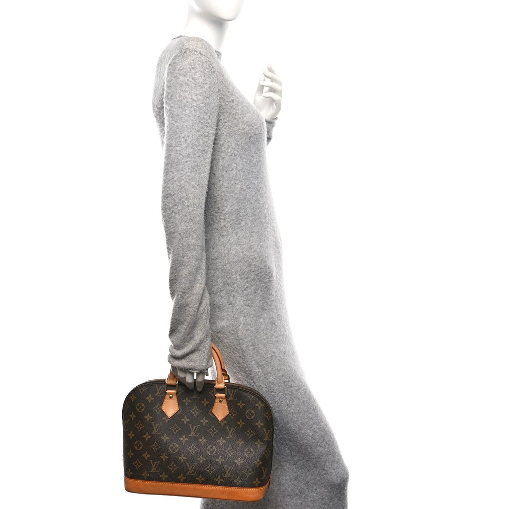 Mannequin wearing a gray sweater holding a brown handbag with monogram pattern.